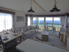 A living room with a sofa, dining table, and ocean view at 619 Chy-An-Mor in Perranporth