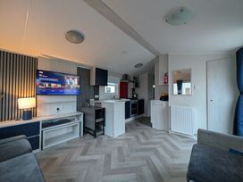 A living room with a tv and kitchen area at Presthaven - Denbigh Dunes in Gronant