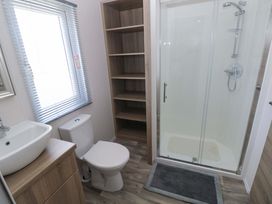 A bathroom with a sink, toilet, shower and shelves at Sandpiper in Narberth