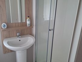 A bathroom with a sink, mirror, soap dispenser, and shower at Primrose Valley, Amara's Retreat, Filey
