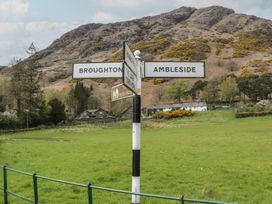 A signpost indicating directions to Broughton and Ambleside near a field and hillside in Coniston