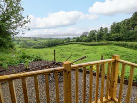 An outdoor view of a grassy field with trees and a wooden deck at The Hut in Llandysul
