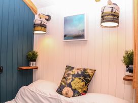 A bedroom with a bed, pillow, plant, light fixture and wall art at Ridden Brake shepherds hut Yelverton