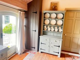 A kitchen with a cabinet displaying plates and a window at The Coach House Cottage in Ballycommon