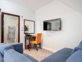 A living room with a sofa, desk, chair, tv, and bathroom door at Cotswolds Apartments 4B/S8 in Chipping Norton
