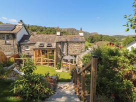 A garden with a stone house and wooden deck at Haws Bank Cottage in Coniston