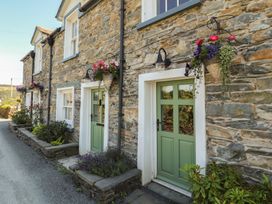 An outdoor view of stone cottages with green doors and hanging flowers at Haws Bank Cottage in Coniston