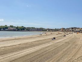 A beach with people walking and sitting at The Watch House in Weymouth