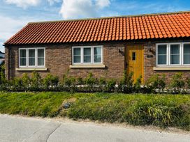 A house with a brick wall and a wooden door at Badger Cottage in Wold Newton