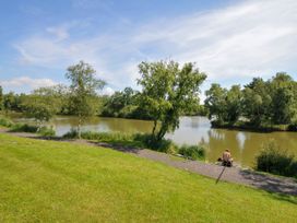 A person sitting near a river with trees and grass at Caravan in Dolton