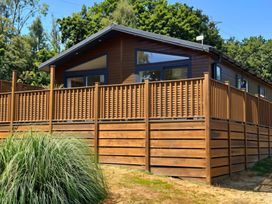 A cabin with a wooden deck surrounded by grass and trees at Lakeside Retreat in Newton Abbot