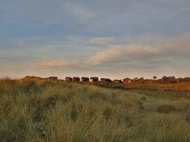 Beach huts on sand dunes under clouds at No 1 The Martins Walberswick