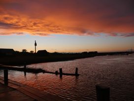 A sunset over water with silhouettes of huts and a post at No 1 The Martins in Walberswick