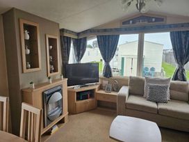 A living room with a sofa and television at a holiday home in a caravan park