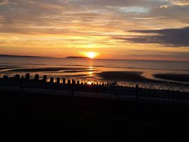 A sunset over the ocean with a beach and fence at Conwy Charm Cottage 3 Bed Retreat Penmaenmawr