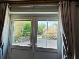 A window with curtains showing a gravel path and stone wall at 