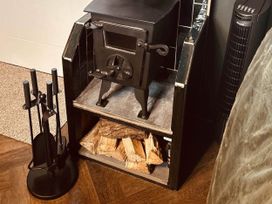 A wood stove with logs and fireplace tools in a living room at The Old Barn in Newton Abbot