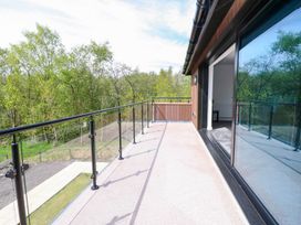 A balcony with a glass railing overlooking trees at Oak Tree Cottage in Frizington