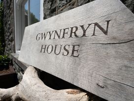 A wooden sign displaying Gwynfryn House outside a stone wall in Llanbedr
