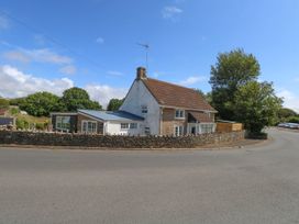 A house with a fence and trees beside the road at Greenwich Cottage in Burton Bradstock