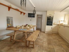 A dining room with a large table, benches and kitchen appliances at Greenwich Cottage in Burton Bradstock