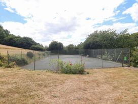 A tennis court with benches and grass at Iris at Stancombe Manor Sherford near Chillington