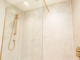 A shower with glass partition and gold fixtures at Hedley Dene Cottage Longhorsley