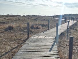 A wooden walkway in a grassy area with wind turbines in the background at Haven Seashore, Ellerton Willerby Xtra, Great Yarmouth