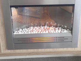 An electric fireplace with stones and a glass front at Seaside Lodge Retreat in Eyemouth