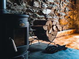 A living room with a wood stove and stacked firewood at The Milking Shed at Pencraig Pet Friendly near Holyhead