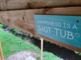 A sign that says 'Happiness is a Hot Tub' in an outdoor area near a stream and grass at Min yr Afon Cabin Sleeps2 Hot Tub Parking in Gwalchmai