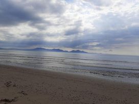 A beach with sand and ocean under a cloudy sky at Gwalchmai