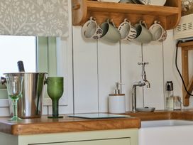 A kitchen with mugs on a shelf and glassware on the countertop at Cosy Luxury Owls Roost Hut with Private Hot Tub near Little Deptford Farm