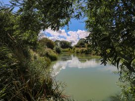 A tranquil scene by the water with trees and clouds at Oak Lodge Battisford near Stowmarket