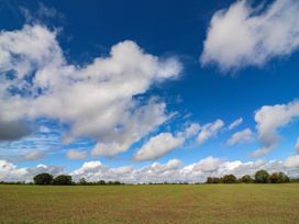 A field with trees under a blue sky with clouds at Oak Lodge Battisford near Stowmarket