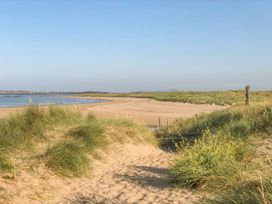 A view of a sandy beach with grass and water at Bryn Tirion - Rhosneigr