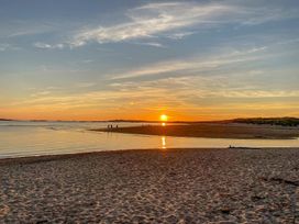 A sunset over water with people walking on the sand at Bryn Tirion - Rhosneigr