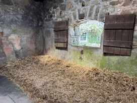 A barn interior with straw on the floor and a window with wooden shutters at Brimble Cottage at Dockwell Farm near Widecombe-In-The-Moor