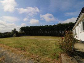 A garden with grass, a gate, and a flower bush at Wilpol in Llanerchymedd