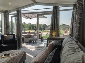 A living room with a sofa and sliding doors leading to outdoor seating at Lakewood Plot 5 St. Osyth
