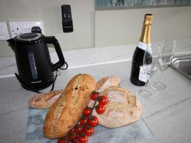 A kitchen with a kettle, champagne, bread, and tomatoes at Cornerhouse Apartment 1 in Llandudno