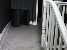 A hallway with a black chair and staircase at Cornerhouse Apartment 1 in Llandudno