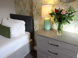 A bedroom with a bed and flowers on a chest of drawers at Cornerhouse Apartment 1 in Llandudno