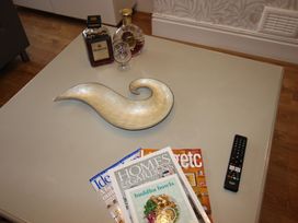 A coffee table with a bowl, magazines, a bottle of liqueur, and a remote control at Cornerhouse Apartment 3 Llandudno