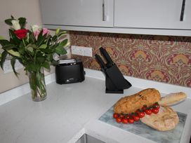 A kitchen with flowers, a toaster, knife block, bread, and tomatoes at Cornerhouse Apartment 5 Llandudno