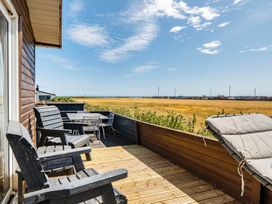 An outdoor terrace with wooden chairs and a table overlooking grass and the sea at 