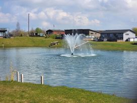 A fountain in a lake with houses behind at Pet Friendly 2Bed Luxury Lodge in Routh HotTub Heron Lakes Luxury Lodge Park near Beverley
