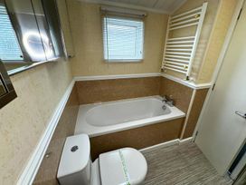 A bathroom with a bathtub, toilet, sink, and mirror at Sunset 5 Southview Holiday Park Skegness