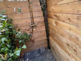 An outdoor shower area with wooden walls and a metal faucet surrounded by ivy at 