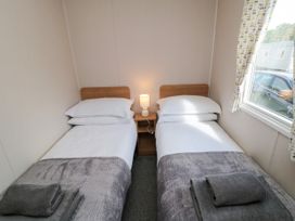 A bedroom with two single beds and a nightstand with a lamp at 14 Pines in Cayton Bay